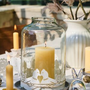 Das Windlicht ist aus dickem Glas gefertigt und deshalb nicht so empfindlich. Für die österliche Note wurde es mit filigranen Papier-Hühnern geschmückt. Auch die restliche Deko harmoniert dazu, alles von Car Möbel.