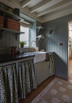 Blumen werden bei der Landhausküche mal ganz anders aufgegriffen, denn es sind die üppigen Vorhänge, die mit den Blätterranken der Küche Persönlichkeit geben. Das ist eine praktische Idee, denn sie können nach Bedarf gewechselt werden, wenn eine andere Optik gewünscht wird. Noch dazu ist es eine Alternative zu typischen Fronten. Stoff von Trove by Studio Duggan.