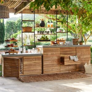 Die Holzkonstruktion der Outdoor-Küche von Loberon begeistert mit ihrem rustikalen Charme und kommt dennoch zeitgemäß daher mit den Boho-Elementen. Auf der großzügigen Arbeitsfläche lassen sich Gerichte gut zubereiten.  