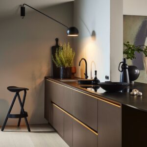 Der puristische Look kann auch mit dunklen Farben in einer kleinen Küche umgesetzt werden. Die offene Raumlösung ist dafür ideal. Durch die Akzentlampe wird sie gezielt ins rechte Licht gesetzt werden. Küche „Soft Lack“ in der Farbe „Sepiabraun“ von Nolte Küchen.