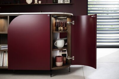 Rund sind hier nicht nur die Außenformen, auch die Fronten als solche haben Schwung. Im Zusammenspiel mit den dunklen Farbtönen sieht das super elegant aus. Aufgelockert wird alles durch offene Regale. Aus der Serie „Curve“ von Schmidt Küchen.