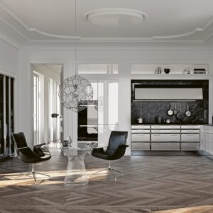 Die Küche „Classic“ von SieMatic ist eine elegante Wahl. Sie ist ganz interessant eingebettet in eine Nische. Das lässt den großen Raum noch größer erscheinen. Auf den ersten Blick erscheint die Edelstahlfront wie in einer Großküche, so ausladend ist sie. Stilvoll sind dazu die weißen, glänzenden Fronten.