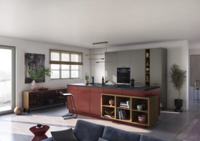 Die Kücheninsel fällt sofort ins Auge. Sie begeistert mit dem attraktiven Rotton. Er bildet einen gelungenen Kontrast zum Grau. Holz- und Golddetails schmeicheln dem Ganzen. Die Möbel sind von Küche & Co.