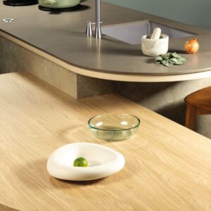 Das neue Hightech-Material „Obisiana“ von Dekker besteht komplett aus recyceltem Glas gemischt mit Harz. Daraus werden Küchenarbeitsplatten hergestellt, die quasi endlos wiederverwendet werden können. Wunderschön ist das Dekor „Volcano Warm“. Der warme, graue Betonton wirkt durch ein sehr feines Muster edel. Auffällig und sehr geschmackvoll ist die Kombination mit der Holzplatte, beides mit angesagten Rundungen.