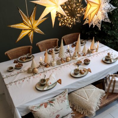 Die festliche Tafel zeigt eine warme, natürliche Weihnachtsstimmung mit zarten Cremetönen und Goldakzenten. Miniatur-Tannenbäume, filigrane Kerzenhalter und dezente Kugeln bilden ein harmonisches Arrangement auf der bestickten Tischdecke. Keramikgeschirr in Naturfarben, goldene Details und Papiersterne vollenden den gemütlich-eleganten Look. Alles von Chic Antique.