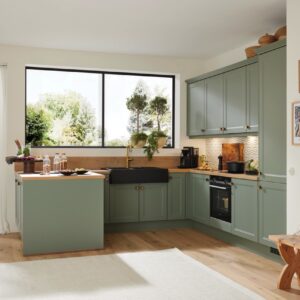 Küche „Camo“ von Mondo zeigt sich in mattem “Schilfgrau” in Lacklaminat. Das verleiht dem Cottage-Stil neue Frische. Auch die typischen Rahmenfronten sehen durch die klaren Linien modern aus. Edel ist die Kombi mit dem schwarzen Keramikbecken plus goldfarbener Armaturen. 