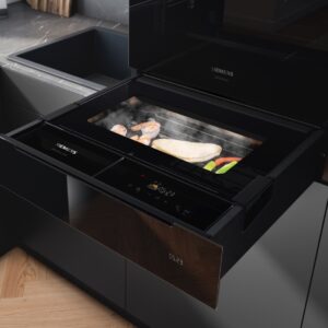 Siemens kombiniert auf minimalem Raum intelligente Technologie mit Design für mehr kulinarische Vielfalt. Die grifflose Schublade aus schwarzem Glas kann entweder mit einem Ofen kombiniert oder einzeln platziert werden. Dadurch erweist sie sich als große Unterstützung für alle, die gesund kochen möchten, ohne viel Platz dafür zur Verfügung zu haben. Über das in der Schublade integrierte Farb-Touch-Display können Temperatur und Zeit präzise von Hand eingestellt werden. Auch stehen zehn Automatikprogramme direkt am Gerät und 20 weitere über die Siemens Home Appliances App zur Verfügung.