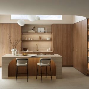 Die abgerundete Insel ist das Highlight in der Küche „Firenze“, denn sie ermöglicht es, bequem daran zu sitzen, ohne eingeschränkte Beinfreiheit und trotzdem eine großzügige Arbeitsfläche zu haben. Das ist eine raffinierte Idee. Die Küche im Holzton „Light Fox“ und „Travertin Valencia“ ist von Schmidt. Spannend ist außerdem die seitliche Regallösung.