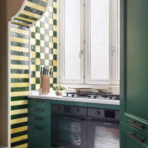 Die Küche von Schmidt ist mal anders gedacht mit ihrer Platzierung in einer Nische. Dazu erscheint sie wie auf einer Bühne durch ihre Umrandung mit den glänzenden Fliesen im mutigen Farbmix. So wird klar, dass auch schlichte Küchen zu einer persönlichen Inszenierung werden können.