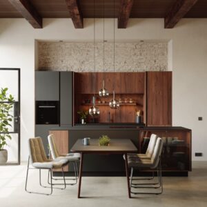 Wie ein Wohnzimmer eingerichtet ist die Küche auf den ersten Blick mit der Zeile im Stil eines Wohnzimmerschrankes und der hübschen Vitrine, die in die Insel integriert wurde. Eine praktische und schöne Lösung ist der Esstisch, der sich direkt an die Insel anschließt. Aus Echtholz, von Walden.