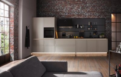 Greige kann auch rustikal. Das beweist diese Küche mit grober Steinwand, industriellen Fenstern und schwarzer Multifunktionsrückwand. Die Küche mit klaren Kassetten-Fronten von Global Küchen mildert den Industrial-Style gekonnt ab.