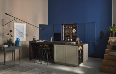 Fast ein bisschen Retro sieht die Gesamterscheinung der Küche aus. Verschiedene Möbelstile werden gemixt, Kühle trifft auf Wärme, Schlichtheit auf Knallfarbe. Absolut gekonnt! Vor allem das ineinander übergehen von Wand und Küchenfronten verdient einen zweiten Blick. Alles von Nolte aus der Linie „Ravenna“ in „Blaubeere“ und „Greige“, beide Töne in „Softmatt“.