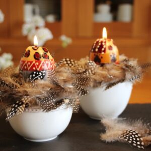 Mit einem Hauch Exotik begeistert das Arrangement mit Kerzen von Nobunto. Die Kerzen werden unter fairen Bedingungen in der Manufaktur in Südafrika hergestellt. Eine süße Ergänzung sind die Federn, die in der Schale drapiert werden.