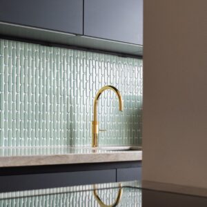 Die tiefblauen Stäbchenfliesen von The Mosaic Factory machen die Küche ganz extravagant. Der Hersteller ist auf Mosaik-Fliesen spezialisiert. Durch die schmale, vertikale Form gestaltet sich ein feines Linienbild, das die Fläche dynamisch und gleichzeitig elegant wirken lässt. Je nach Lichteinfall wechseln die glänzenden Oberflächen zwischen satten Farbnuancen und spiegelnden Reflexen und schaffen so einen reizvollen Kontrast zu Holz und dunklen Arbeitsflächen.
