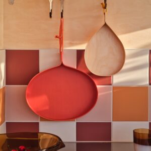 Aufhängen statt verstauen: An der „Hultarp“ Stange von IKEA bleiben Servierbretter griffbereit und werden zugleich zum Wandschmuck. Vor dem Fliesenspiegel in Orange, Rosa und Rot kommen sie besonders gut zur Geltung.