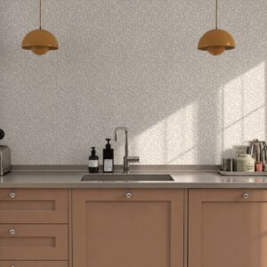 Die Tapete „Vinda“ von Lycke über Happy Homes sorgt mit ihrem feinen Blättermuster für eine zurückhaltende Note in die Küche. Senfgelbe Pendelleuchten setzen dazu kleine, aber wirkungsvolle Farbakzente. Die Fronten im Karamellton haben eine herbstliche Ausstrahlung