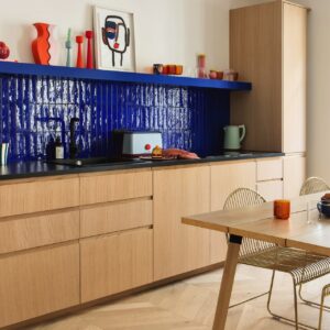 Plum Living verbindet helle Holzfronten mit einem leuchtend blauen Fliesenspiegel und beweist damit, wie optimal Naturmaterialien und kräftige Farben zusammenwirken können. Die warme Holzoptik nimmt der intensiven Farbgestaltung ihre Strenge. Gelungen ist das Zusammenspiel aus handwerklicher Anmutung und moderner Linienführung.