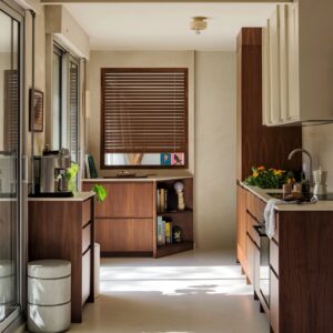 Hersteller Plum Living kombiniert dunklen Nussbaum mit hellen Wandflächen. Das ergibt einen beeindruckenden Kontrast. Die durchgehenden Fronten und die waagerechte Maserung verleihen dem schmalen Raum Ruhe und Struktur. Das Holz bringt eine schöne Stimmung in die geradlinige Architektur und lässt die Küche zeitlos aussehen.